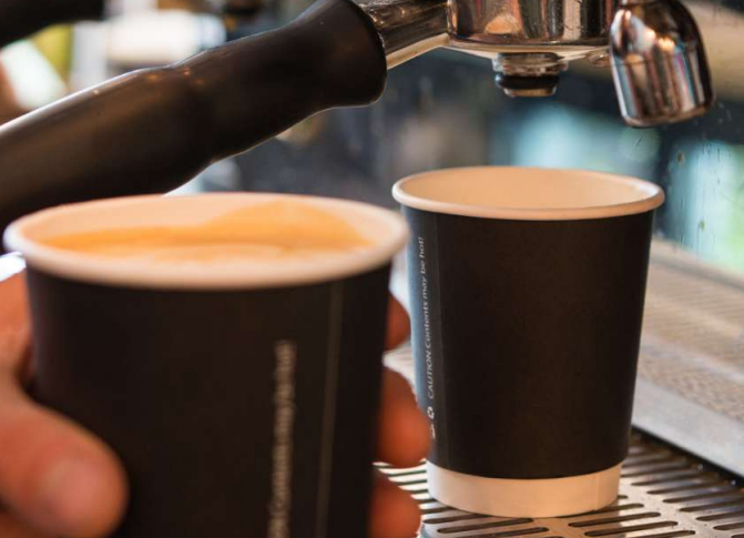 Two double wall black coffee cups with, one containing a latte. 