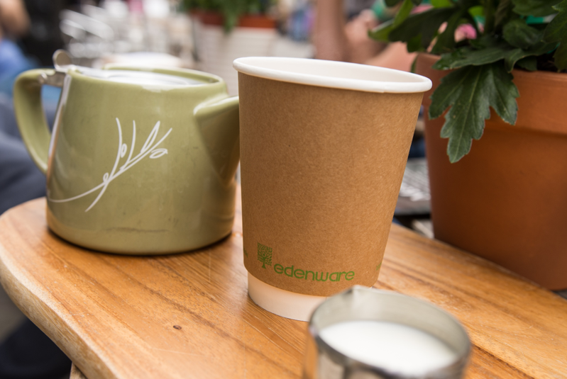 A kraft edenware takeaway coffee cup sitting next to a green teapot.